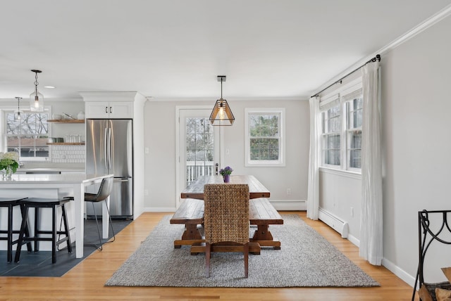 dining space featuring a baseboard heating unit, a wealth of natural light, baseboards, and light wood finished floors