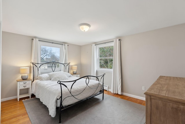 bedroom with baseboards, light wood-style floors, and a baseboard heating unit