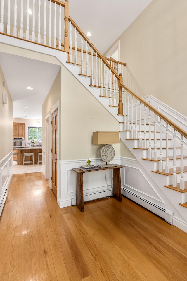 148 Hunter Way, Falmouth, ME 04105 - stairway featuring wood finished floors, wainscoting, baseboard heating, a decorative wall, and a high ceiling