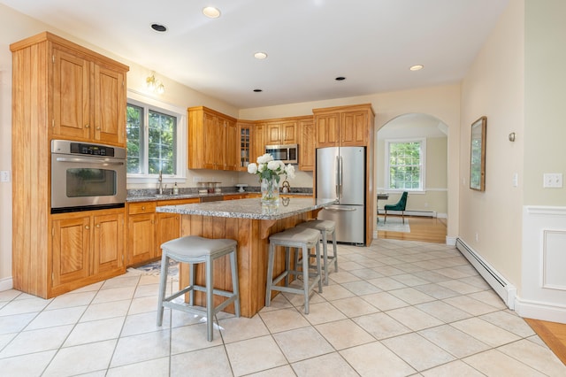 148 Hunter Way, Falmouth, ME 04105 - kitchen featuring appliances with stainless steel finishes, a baseboard heating unit, arched walkways, light stone countertops, and a kitchen island