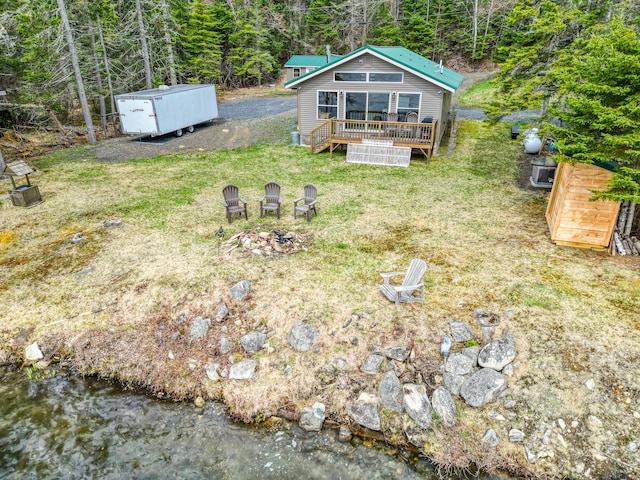 view of green lawn with a deck, a wooded view, and an outdoor fire pit