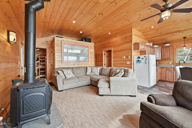 living area with vaulted ceiling, wood walls, a wood stove, wooden ceiling, and a ceiling fan