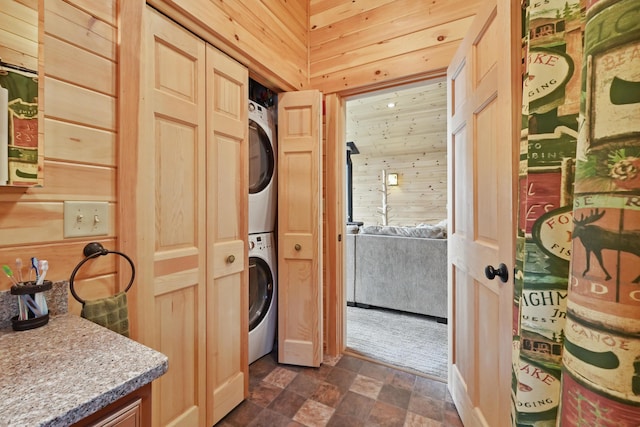 clothes washing area with estacked washer and dryer, stone finish flooring, and wood walls