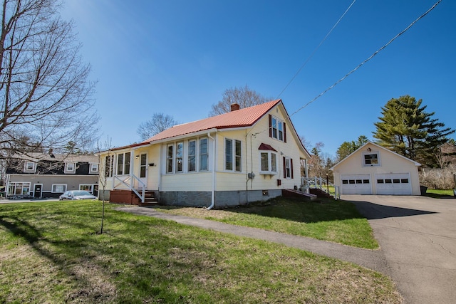 view of front of house featuring a garage, a chimney, metal roof, a front yard, and an outbuilding