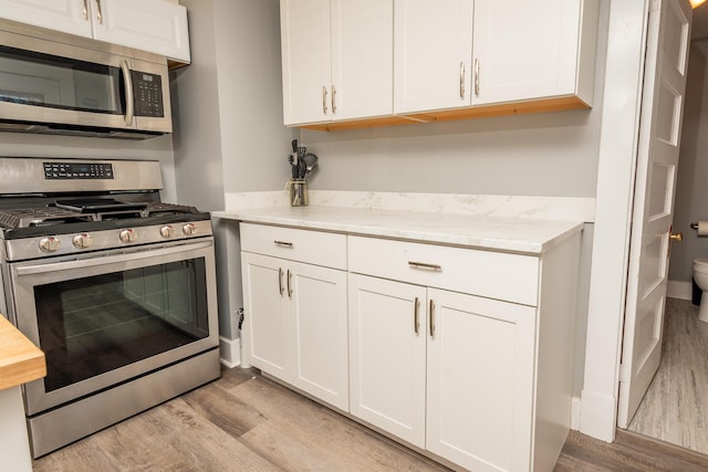 kitchen featuring light wood finished floors, stainless steel appliances, white cabinets, and light stone countertops