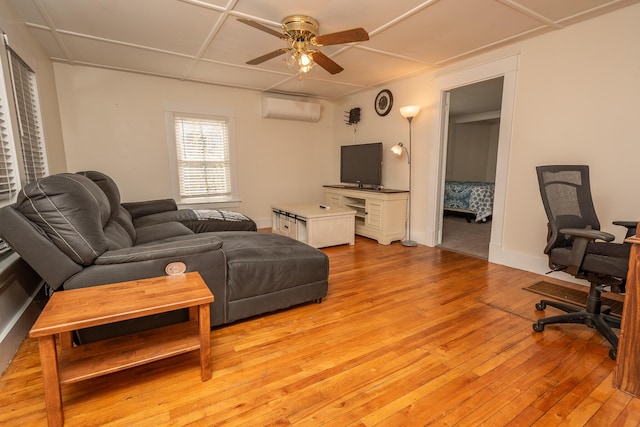 living room featuring a wall mounted air conditioner, light wood-style flooring, and ceiling fan