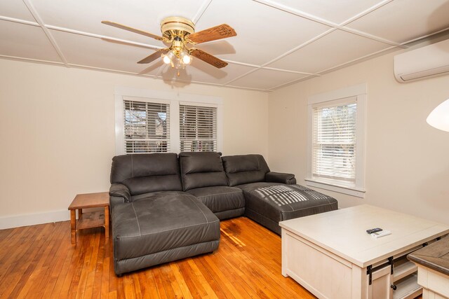 living area with ceiling fan, a wall mounted air conditioner, baseboards, and light wood finished floors