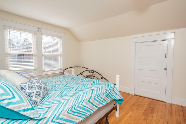 bedroom featuring baseboards, light wood-type flooring, and vaulted ceiling