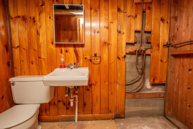 bathroom featuring a sink, toilet, concrete flooring, and wooden walls