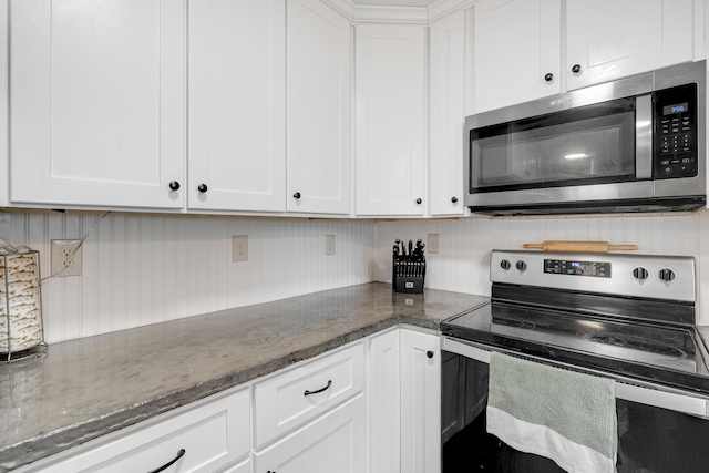 kitchen featuring stainless steel appliances, white cabinetry, and dark stone counters
