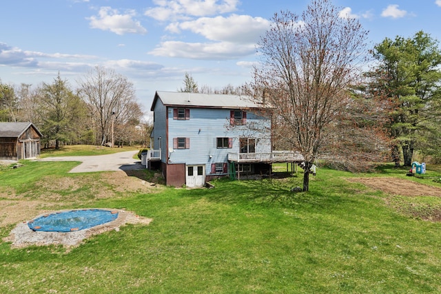rear view of house featuring a yard, a wooden deck, and driveway