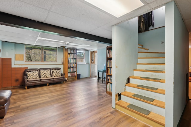 below grade area with a paneled ceiling, wood finished floors, and stairway