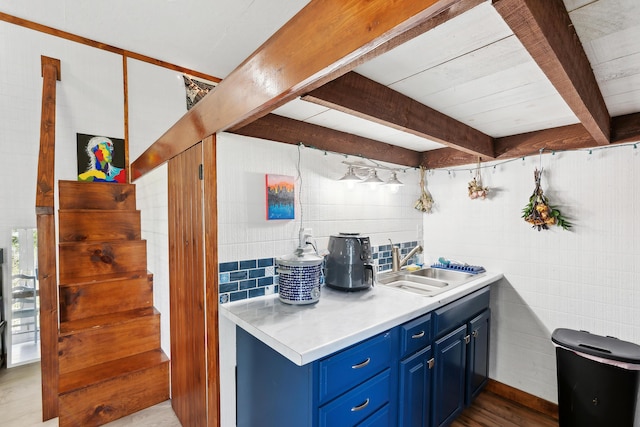 kitchen with blue cabinets, a sink, light countertops, beamed ceiling, and wood finished floors