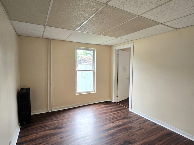 unfurnished room with a paneled ceiling, radiator, dark wood-style flooring, and baseboards