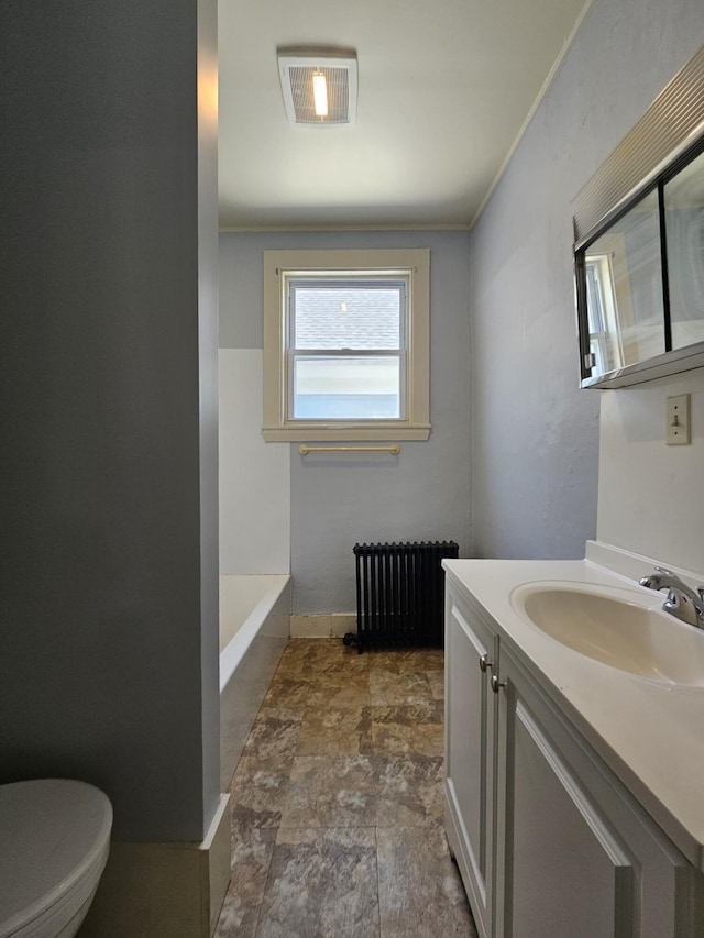 full bathroom featuring radiator heating unit, stone finish floors, toilet, vanity, and a tub to relax in
