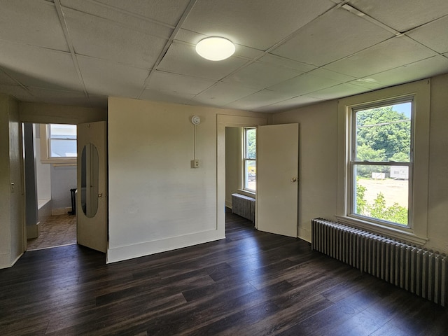 unfurnished room with radiator heating unit, dark wood finished floors, baseboards, and a paneled ceiling