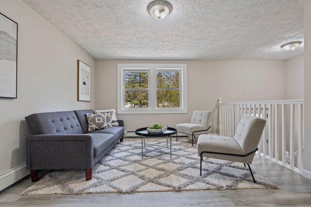 living room with wood finished floors, a textured ceiling, baseboard heating, and baseboards