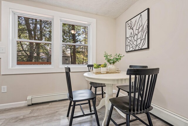 dining space featuring a textured ceiling, baseboard heating, baseboards, and wood finished floors