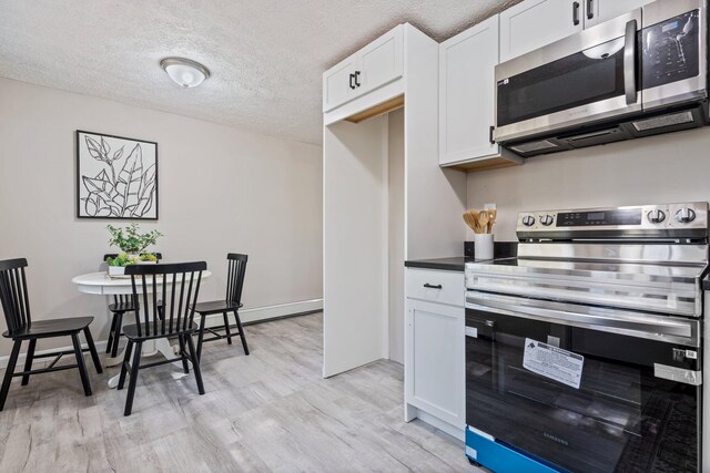 kitchen with appliances with stainless steel finishes, light wood finished floors, a textured ceiling, white cabinets, and dark countertops