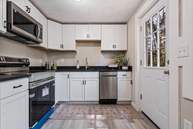 kitchen featuring stainless steel appliances, a sink, white cabinets, light wood-style flooring, and dark countertops