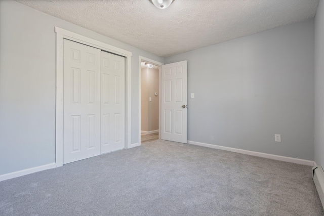 unfurnished bedroom with carpet flooring, a closet, a textured ceiling, and baseboards
