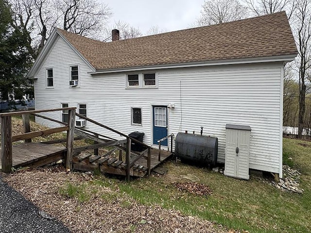 rear view of house featuring a chimney, a deck, roof with shingles, and heating fuel