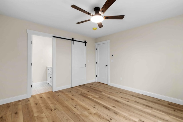26 June St, Sanford, ME 04073 - unfurnished bedroom with light wood-style flooring, a barn door, baseboards, and a ceiling fan