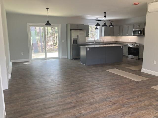 kitchen with open floor plan, baseboards, gray cabinetry, appliances with stainless steel finishes, and a kitchen island