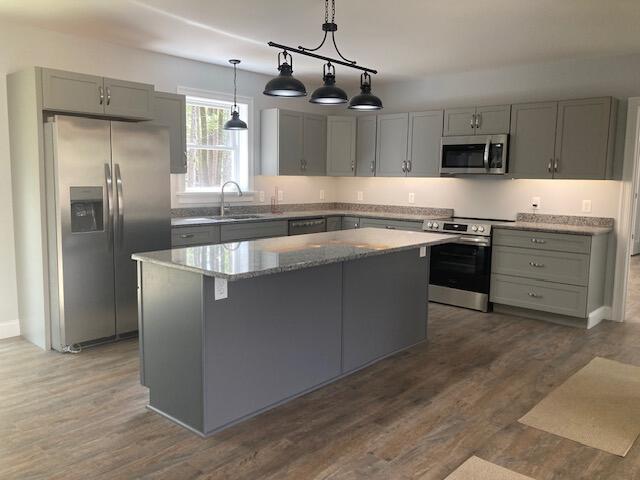 kitchen featuring gray cabinetry, dark wood-style flooring, light stone counters, a kitchen island, and appliances with stainless steel finishes