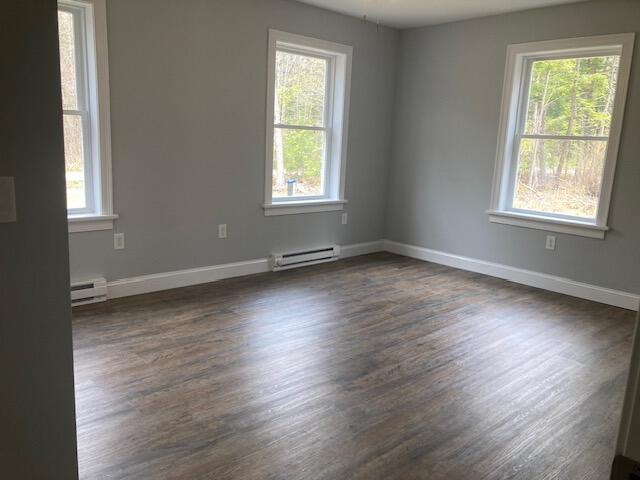 unfurnished room featuring a baseboard heating unit, a wealth of natural light, and dark wood-style floors