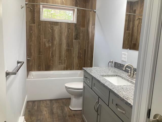 bathroom featuring toilet, wood finished floors, vanity, and shower / washtub combination