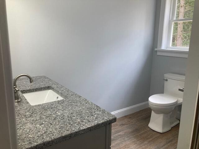 half bathroom with toilet, baseboards, wood finished floors, and vanity