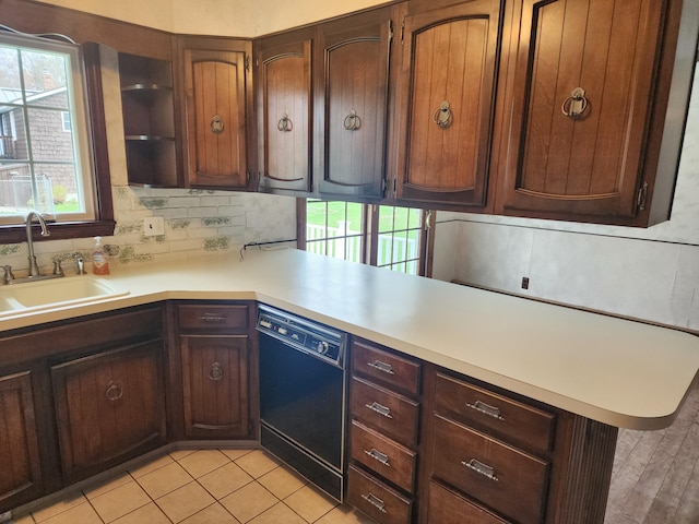 kitchen with a sink, decorative backsplash, light countertops, and black dishwasher