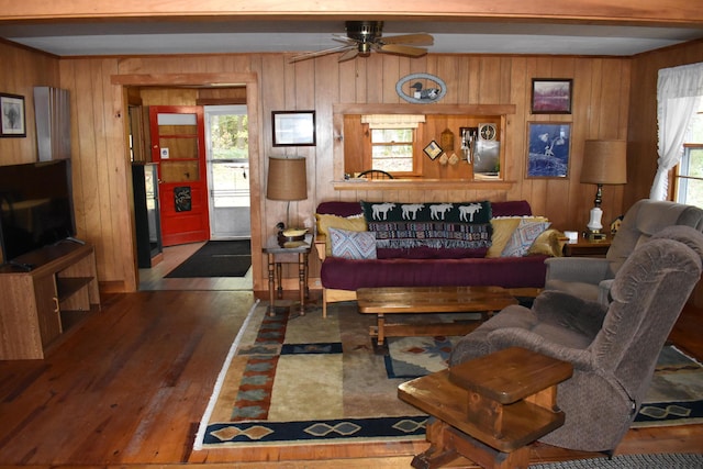 living area with ceiling fan, wooden walls, and wood finished floors