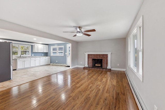unfurnished living room featuring a baseboard heating unit, a fireplace, a baseboard radiator, light wood-style flooring, and ceiling fan