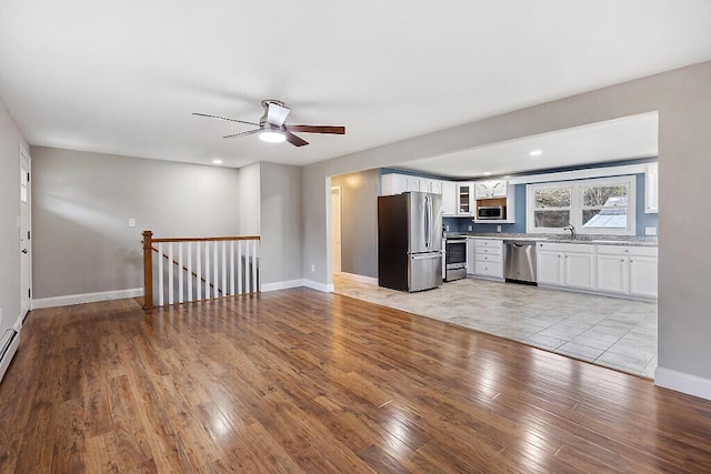 kitchen featuring light wood finished floors, glass insert cabinets, a ceiling fan, a sink, and appliances with stainless steel finishes