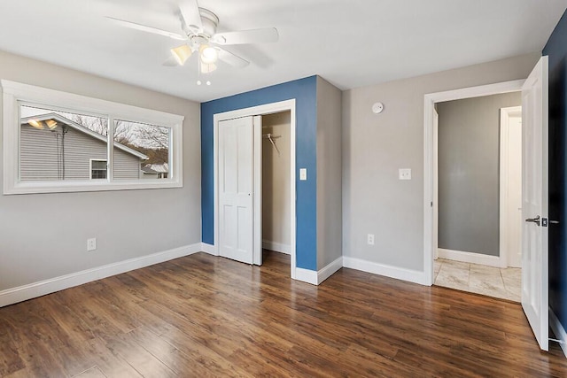 unfurnished bedroom featuring ceiling fan, baseboards, a closet, and wood finished floors