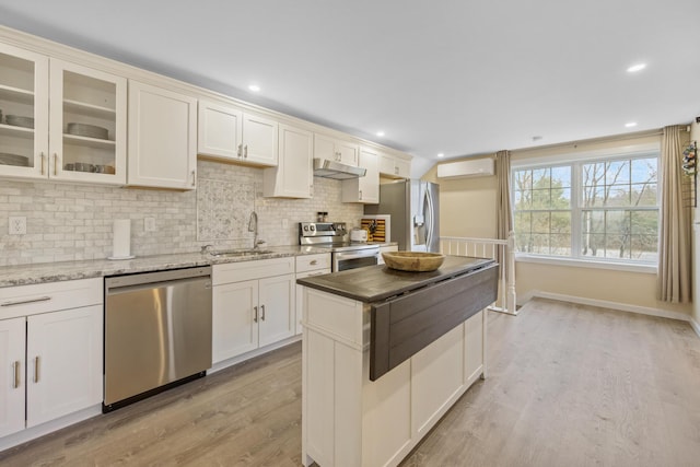 kitchen featuring stainless steel appliances, a sink, under cabinet range hood, a wall mounted air conditioner, and light wood finished floors