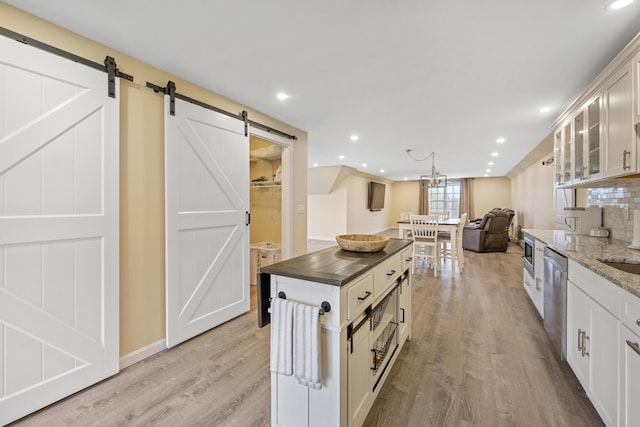 kitchen featuring a barn door, light wood-style flooring, glass insert cabinets, open floor plan, and a kitchen island