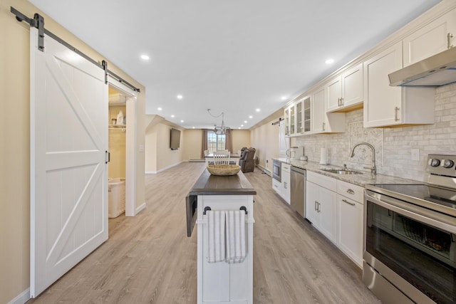 kitchen with stainless steel appliances, a barn door, a sink, decorative backsplash, and light wood-style floors