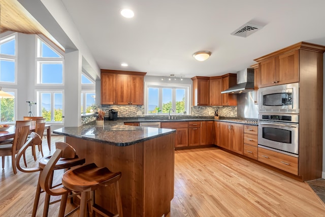 48 White Mountain Way, Bridgton, ME 04009 - kitchen featuring stainless steel appliances, wall chimney exhaust hood, brown cabinetry, plenty of natural light, and recessed lighting