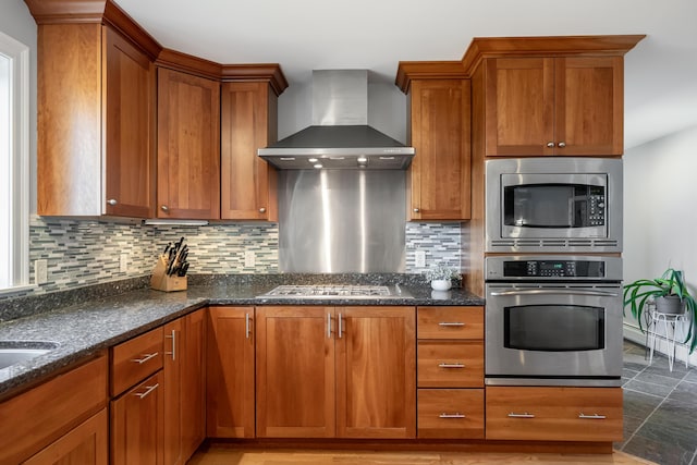 48 White Mountain Way, Bridgton, ME 04009 - kitchen with appliances with stainless steel finishes, wall chimney exhaust hood, brown cabinetry, decorative backsplash, and dark stone counters