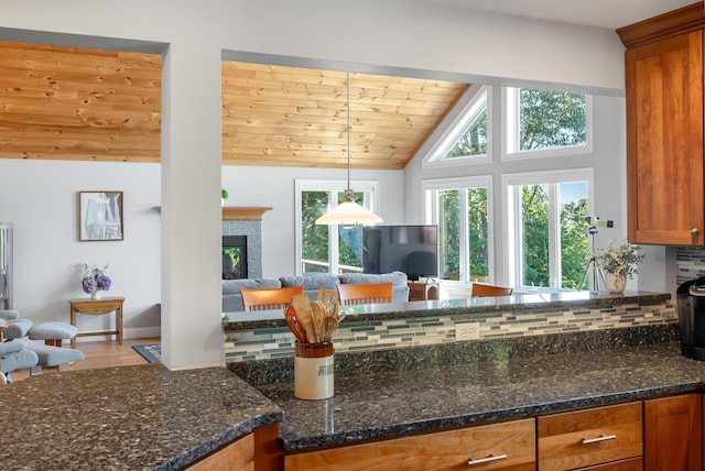 48 White Mountain Way, Bridgton, ME 04009 - kitchen with open floor plan, brown cabinets, lofted ceiling, backsplash, and a glass covered fireplace