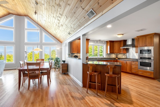 48 White Mountain Way, Bridgton, ME 04009 - kitchen featuring appliances with stainless steel finishes, wall chimney range hood, brown cabinets, dark countertops, and vaulted ceiling