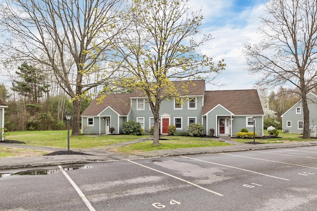 view of front facade with uncovered parking, roof with shingles, and a front yard