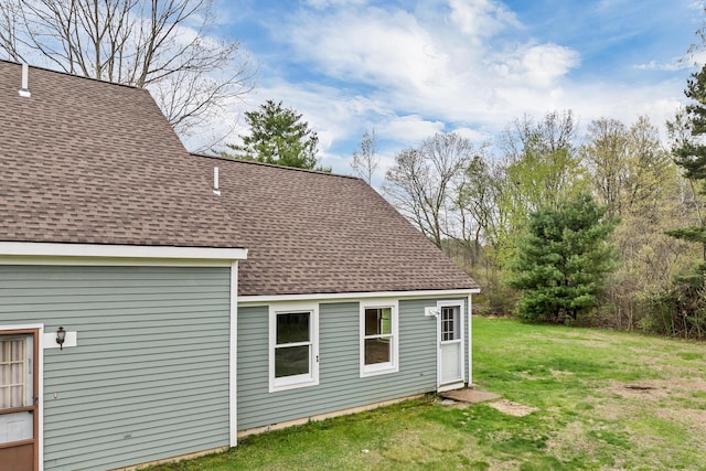 back of property with a shingled roof and a lawn