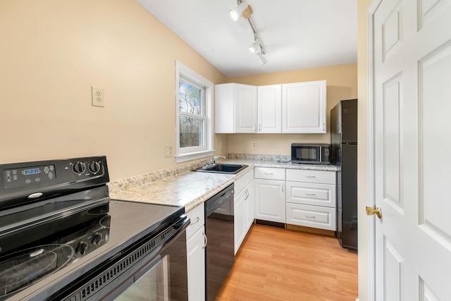 kitchen with a sink, black appliances, light wood-style flooring, light countertops, and white cabinets