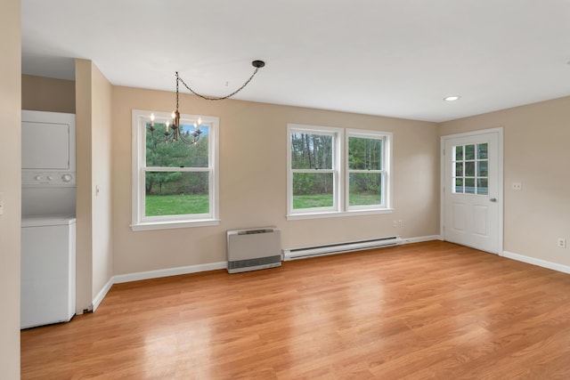 unfurnished dining area featuring a baseboard radiator, heating unit, an inviting chandelier, stacked washing maching and dryer, and baseboards
