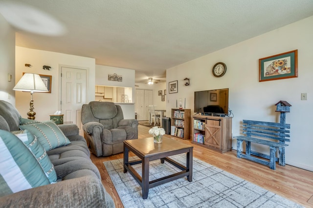 living area featuring light wood-style flooring, a ceiling fan, a textured ceiling, and baseboards