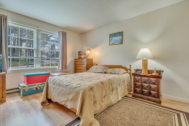 bedroom with a baseboard radiator, wood finished floors, and baseboards